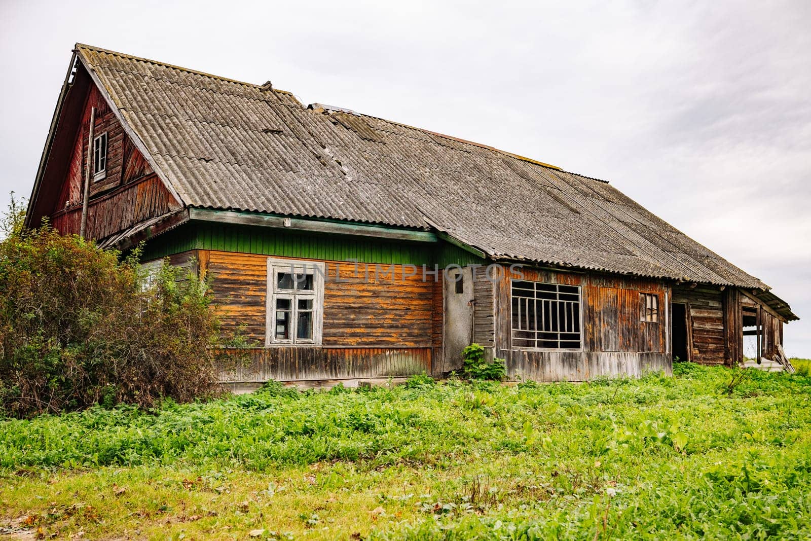 Old ruined wooden house with broken windows and damaged roof is collapsing in countryside field