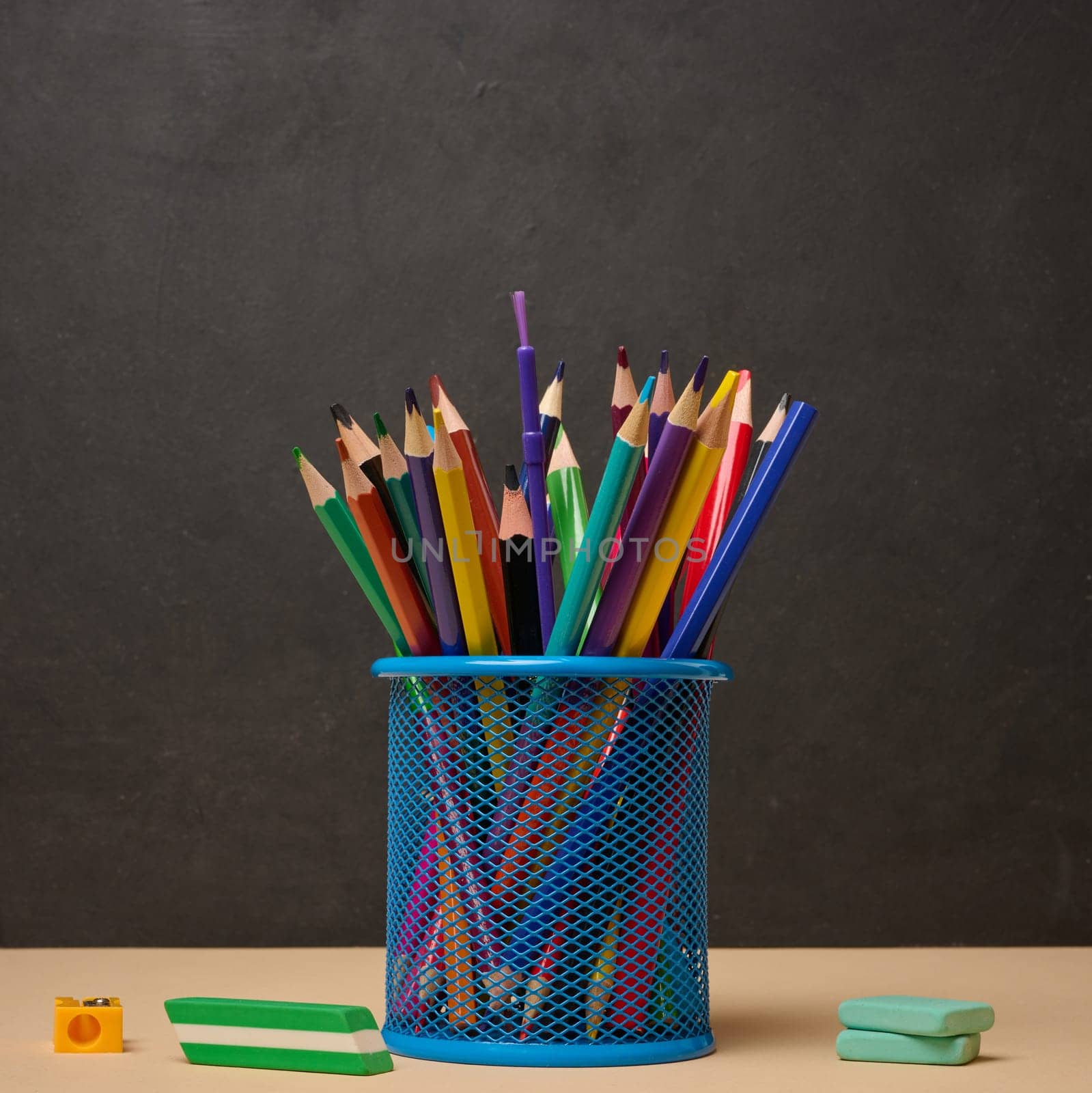Multi-colored pencils in a blue metal cup, sharpener and erasers symbolizing study or creativity