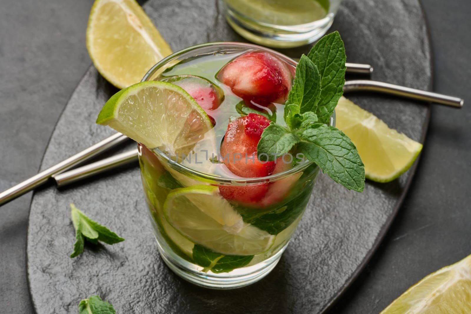 Refreshing mojito cocktail with lime, mint, strawberry, and ice on dark background, top view