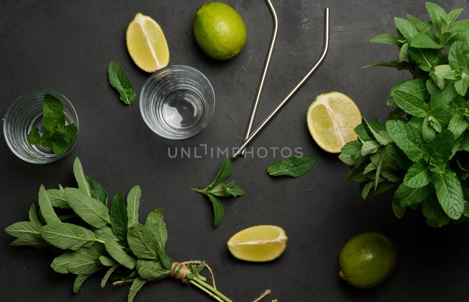Bunch of fresh green mint on wooden table and lime wedges, glasses and metal straws, top view. Cocktail ingredient