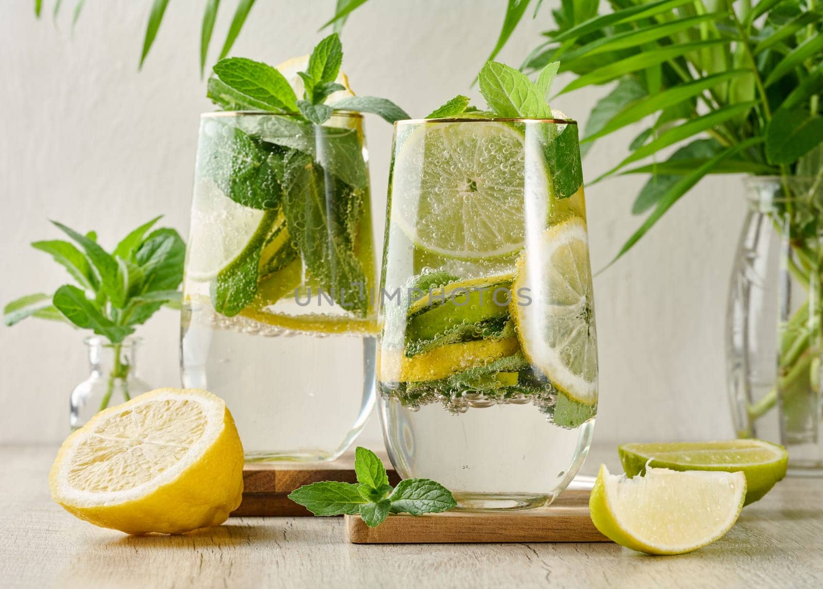 Refreshing citrus and mint drink in glasses with ice, lemon, lime, and mint leaves. Healthy summer beverage