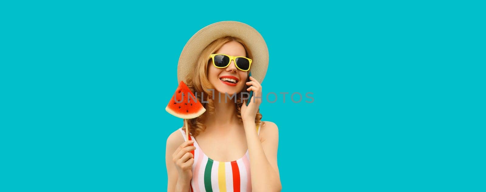 Summer vacation, happy joyful woman calling on phone with fresh fruits, lollipop or ice cream slice of watermelon, wear tourist hat, cheerful girl talking on smartphone on blue studio background