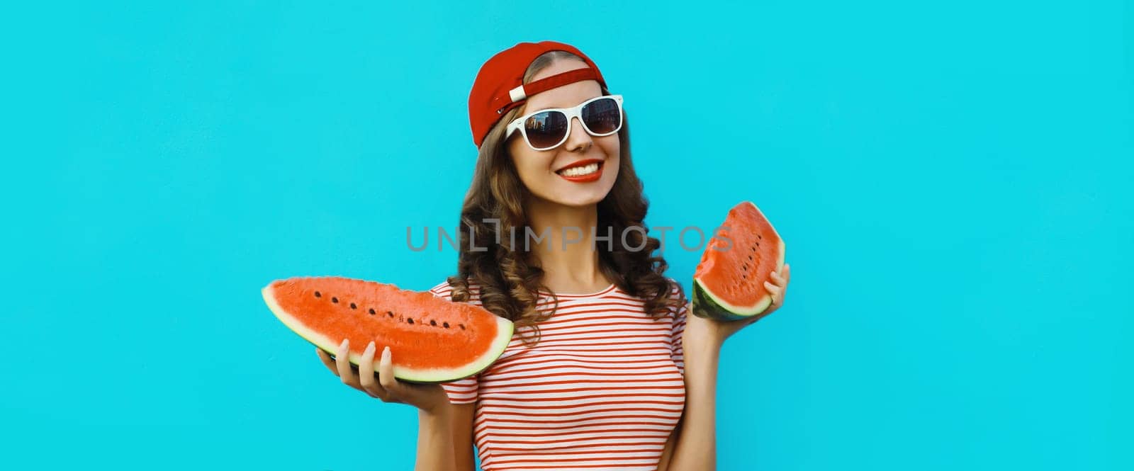 Summer portrait of happy young woman eating fresh slice of watermelon on blue studio background