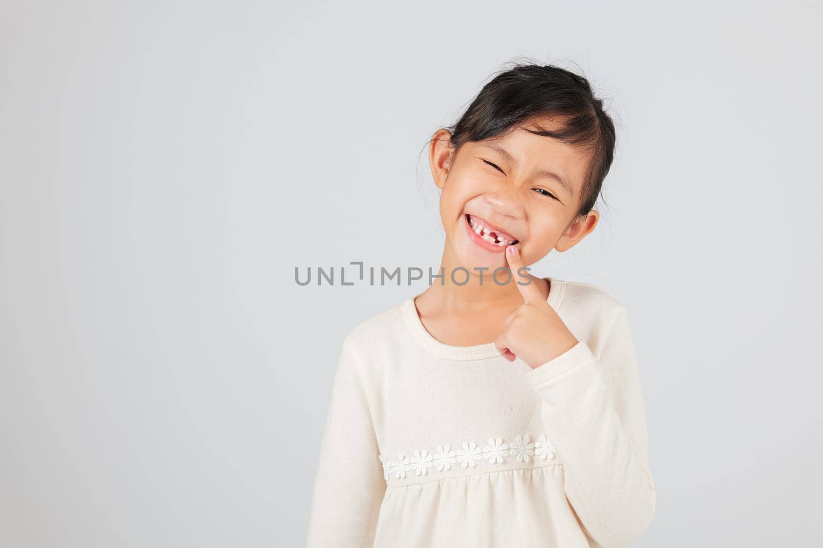 A happy child showcases a tooth gap by pointing at it. The dentist helps kids understand the stages of tooth loss and how to care for their growing tooth gap.