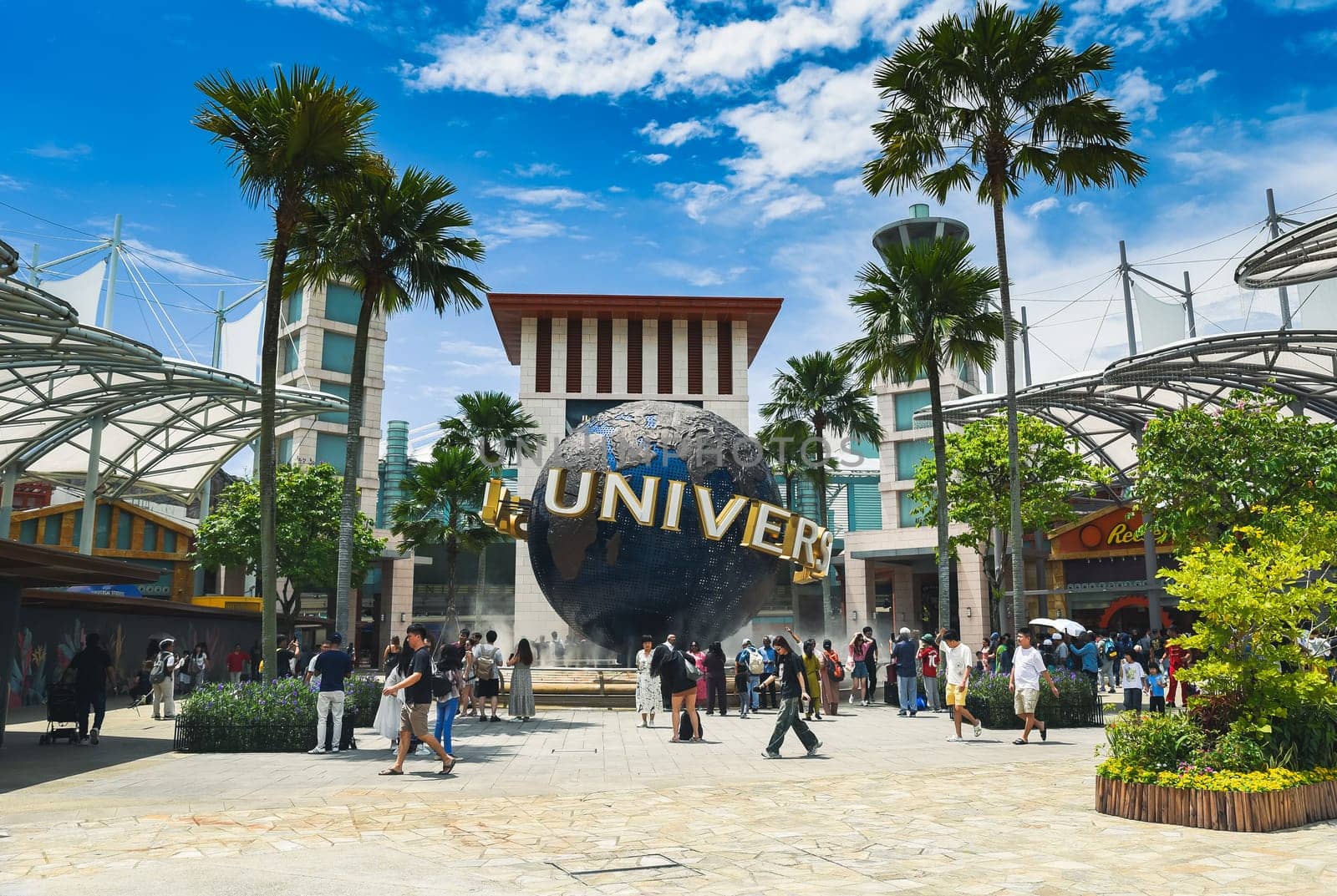 Singapore, Singapore – 4 April 2025: Visitors gather around the iconic Universal globe on Sentosa Island beneath clear blue skies and swaying palm trees.
