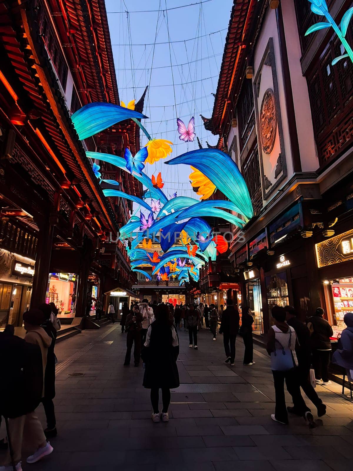 Shanghai, China - 1 April 2025: Colorful illuminated decorations with flowers and butterflies above Yuyuan Old Street in Shanghai during evening walk