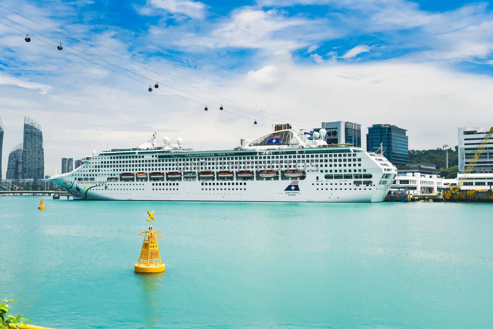 Singapore, Singapore - 4 April 2025: Star Voyager cruise ship docked at Sentosa Island terminal with cable cars above and city skyline in the background.