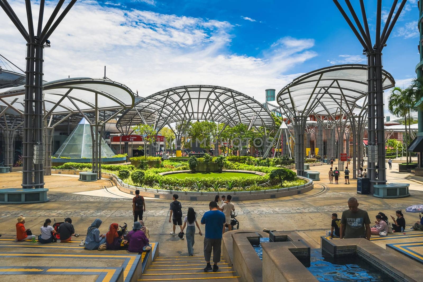 Singapore, Singapore - 4 April 2025: People walk and relax near canopy structures at Resorts World Sentosa plaza on Sentosa Island under blue sky