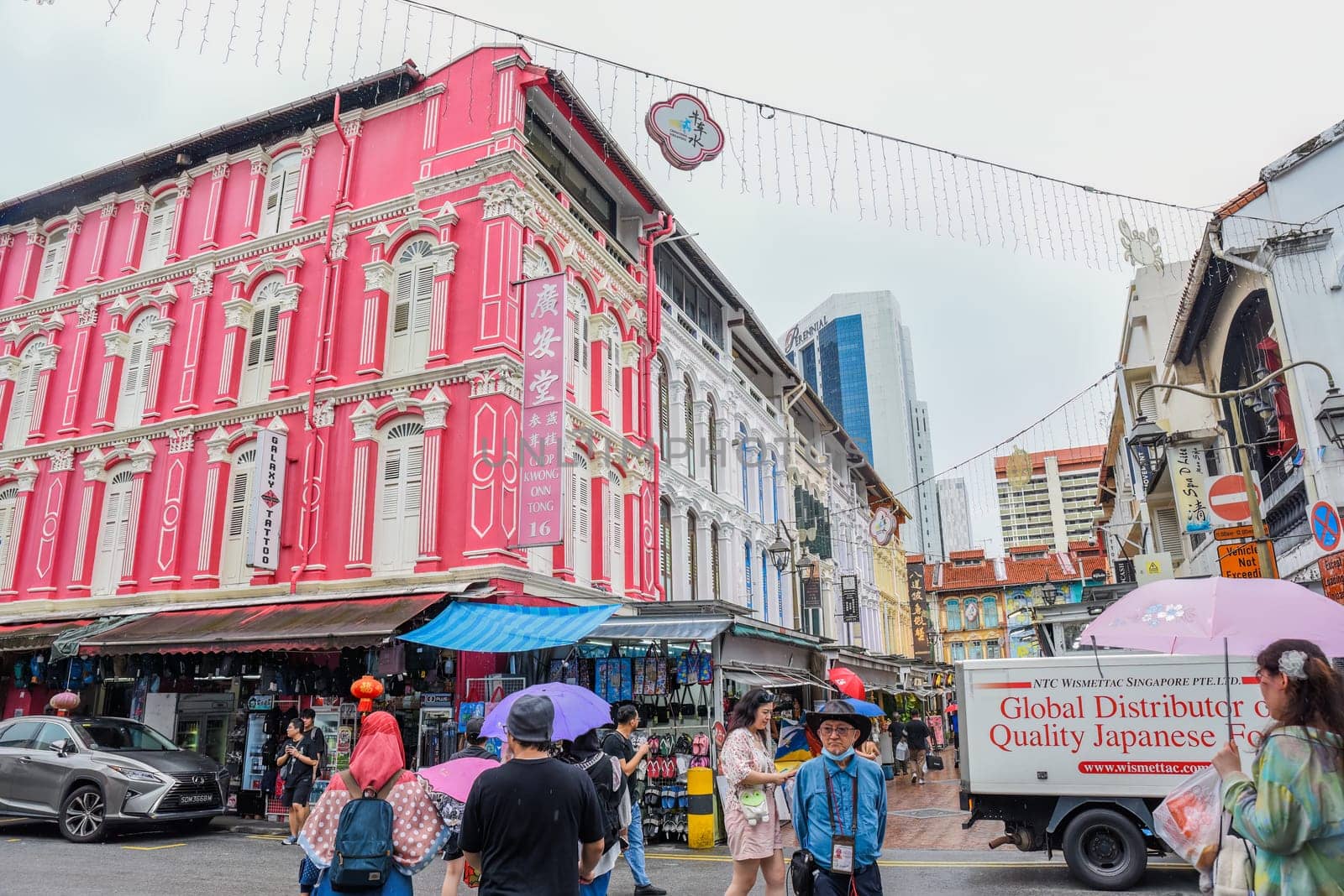Singapore, Singapore - 4 April 2025: Colorful colonial buildings and street life in Little India. People walking with umbrellas on a rainy day in a vibrant urban scene.