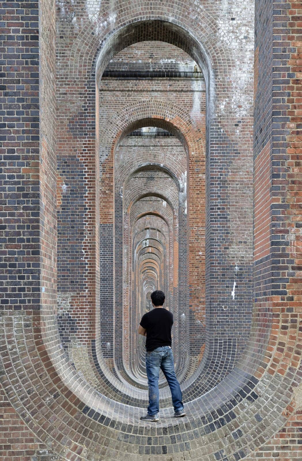 Sussex, UK - May 21, 2025 - Back view of a young man wearing a black T-shirt and jeans standing on the structure under the bridge of Ouse Valley Viaduct or Balcombe Viaduct, has been described as “the most elegant viaduct in Britain” use it as your Wallpaper, Poster and Space for text, Selective focus.