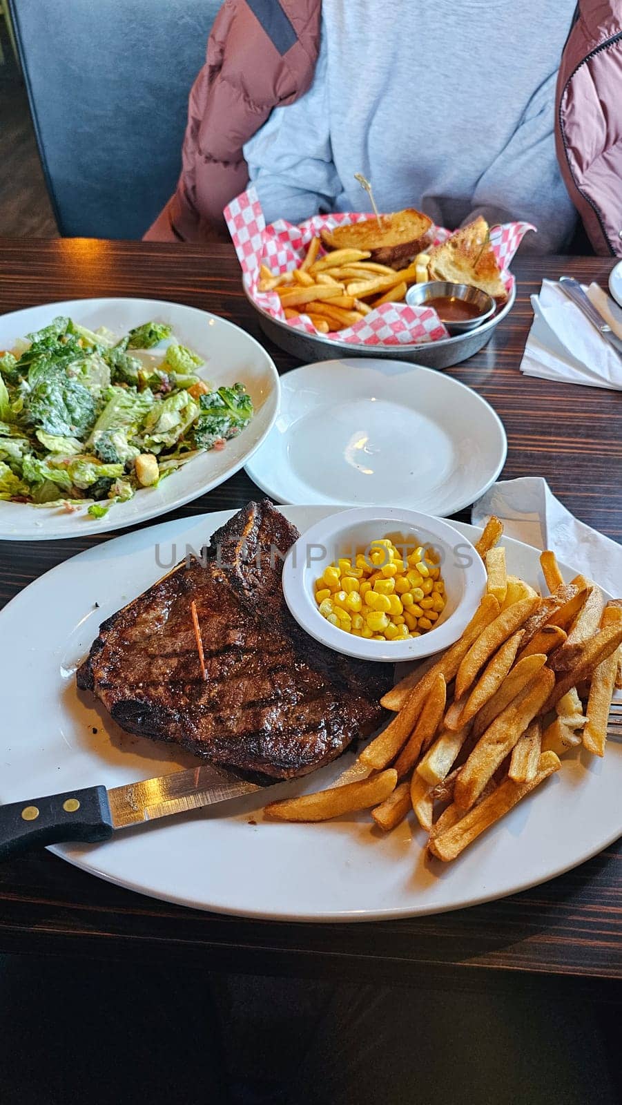 Savor a delicious steak dinner with a tender, grilled steak, a fresh garden salad, crispy French fries, and sweet corn. A perfect meal for food lovers and culinary enthusiasts.