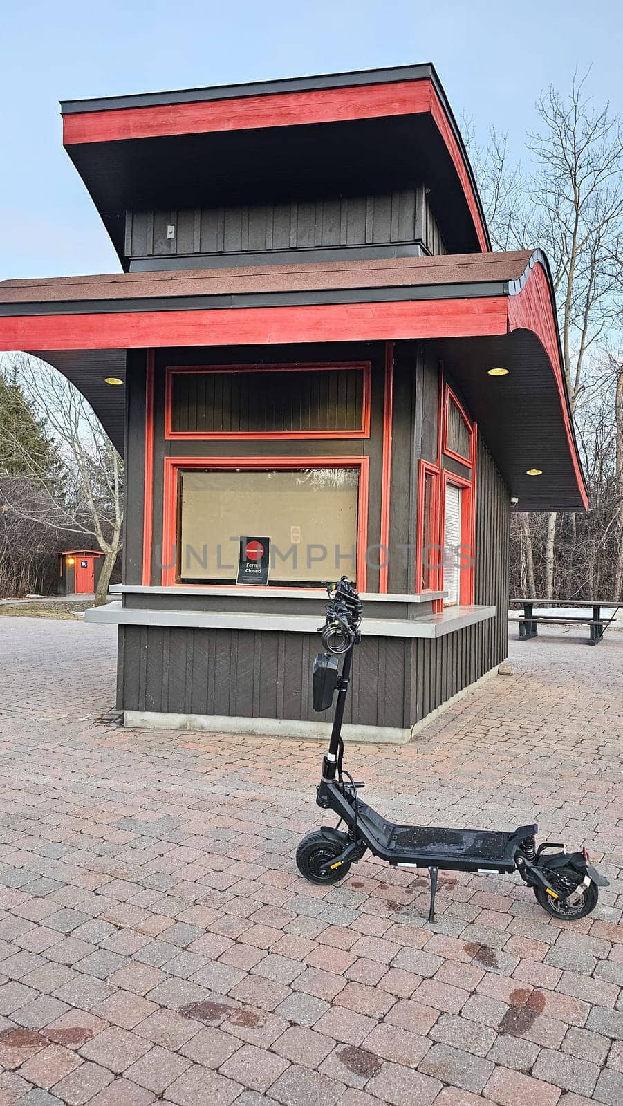 An electric scooter is parked on a brick-paved area near a closed concession stand. This urban scene highlights transportation and recreation in a city outdoor setting.