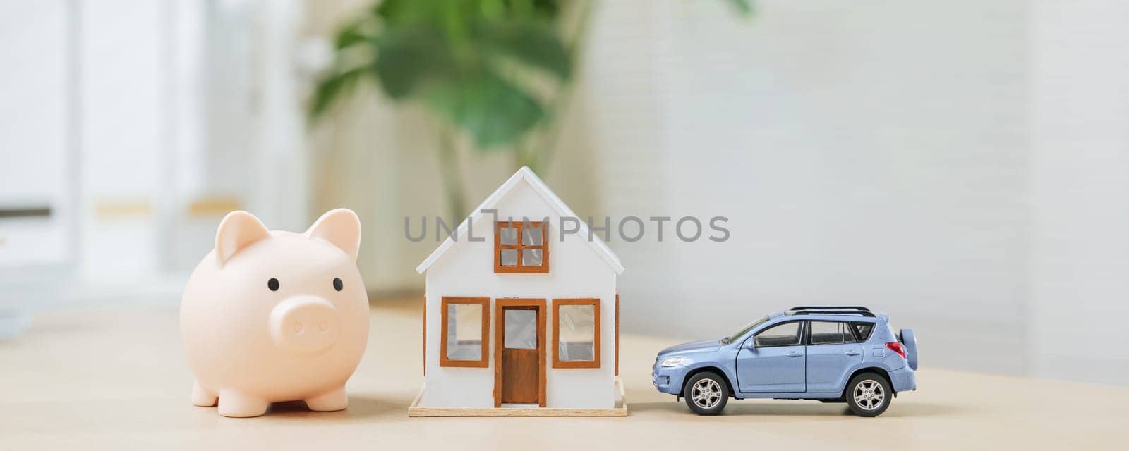A piggy bank and blue car next to a house highlight property investment and saving. Concepts of asset building, financial planning, and expense management for realizing home and car ownership goals.