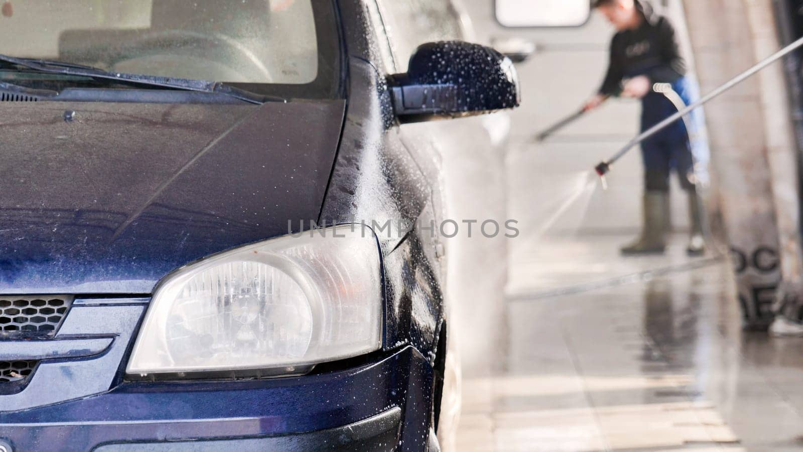 Car wash worker spraying foam and cleaning vehicle with high pressure water jet