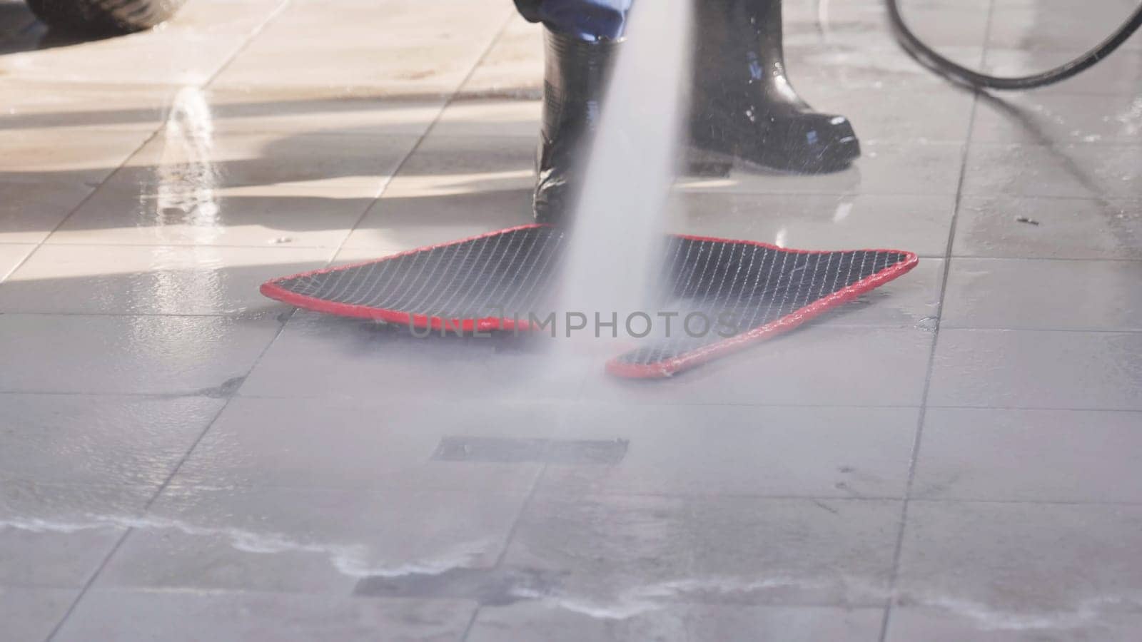 Car wash worker using high pressure water jet to clean car mat