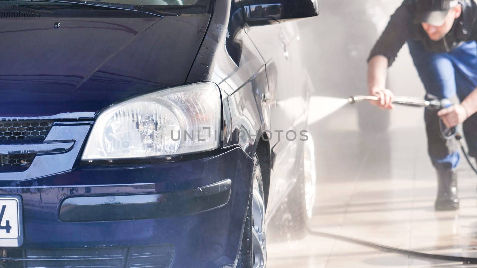 Professional car wash worker cleaning dark blue vehicle with high pressure water jet