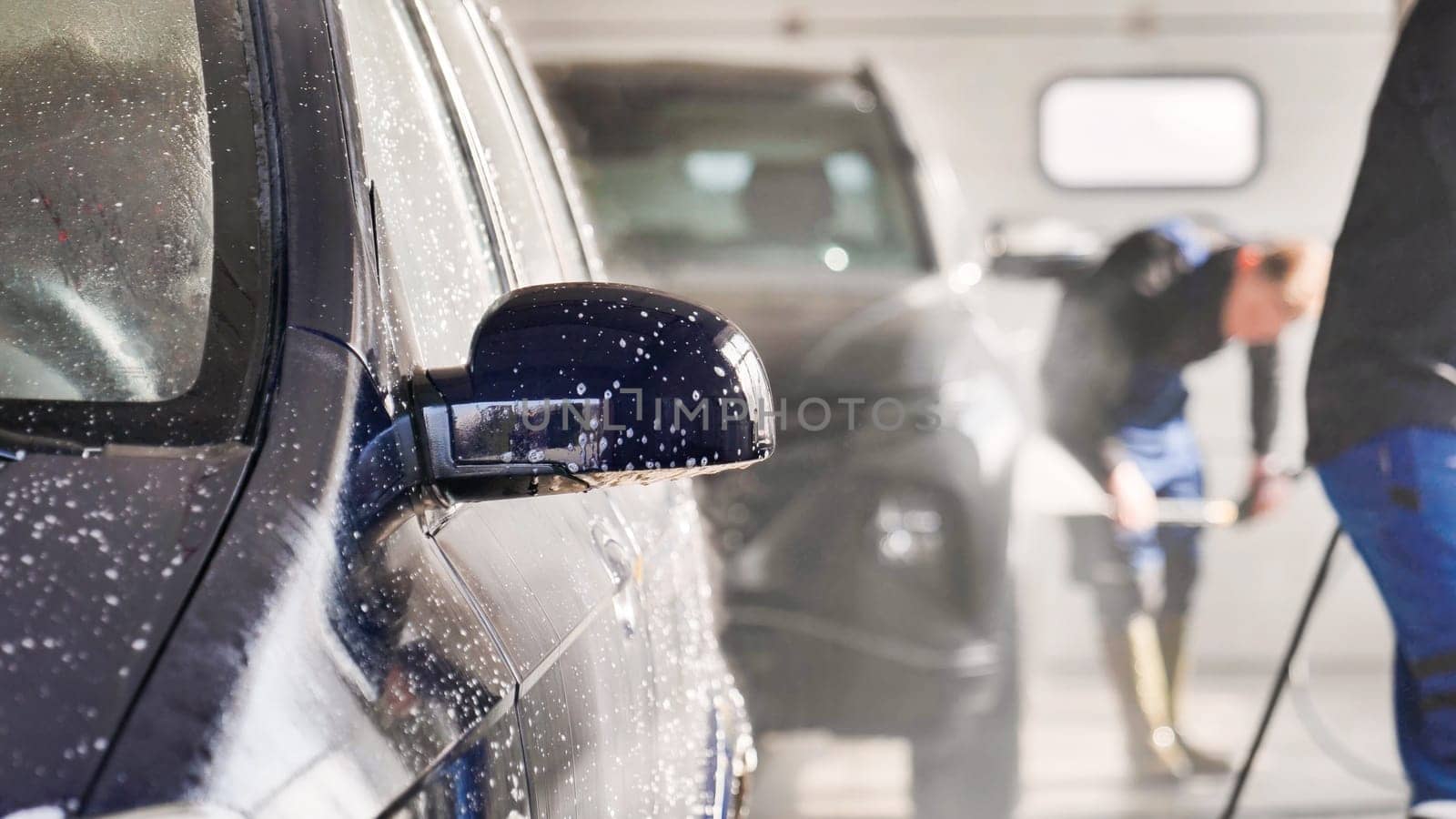 Car wash workers cleaning vehicle with high pressure water jet in a professional car wash