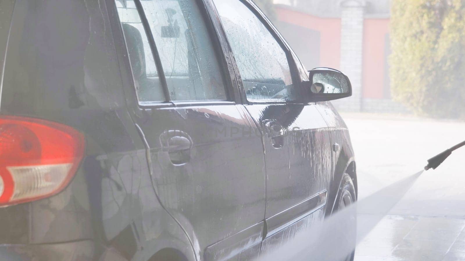 Car wash worker cleaning vehicle with high pressure water jet