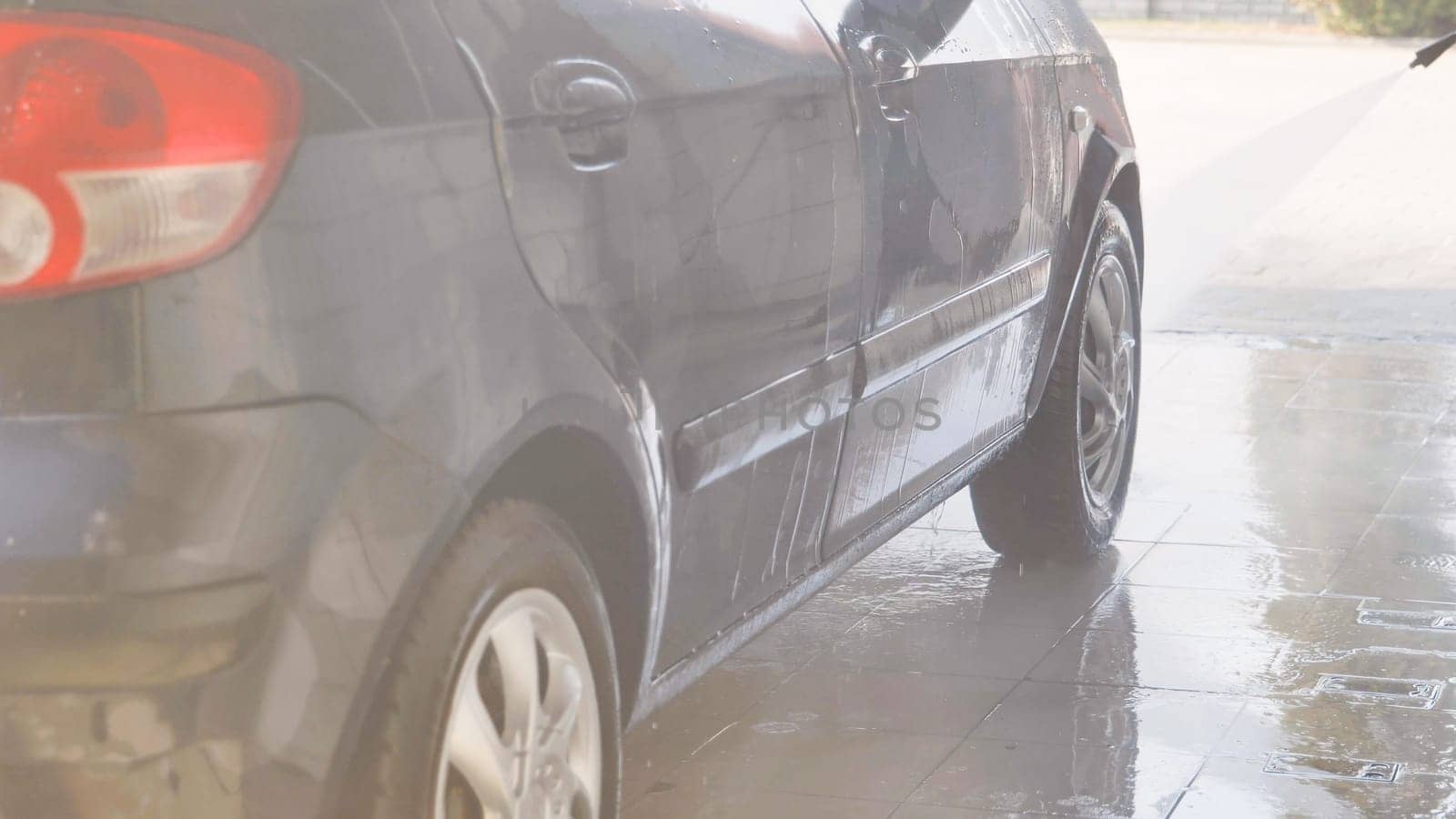 Car wash worker cleaning gray car with high pressure water jet