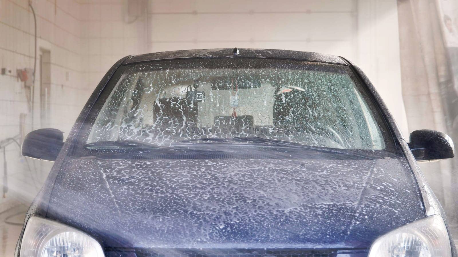 Car is being washed with soap and high pressure water jet in carwash station