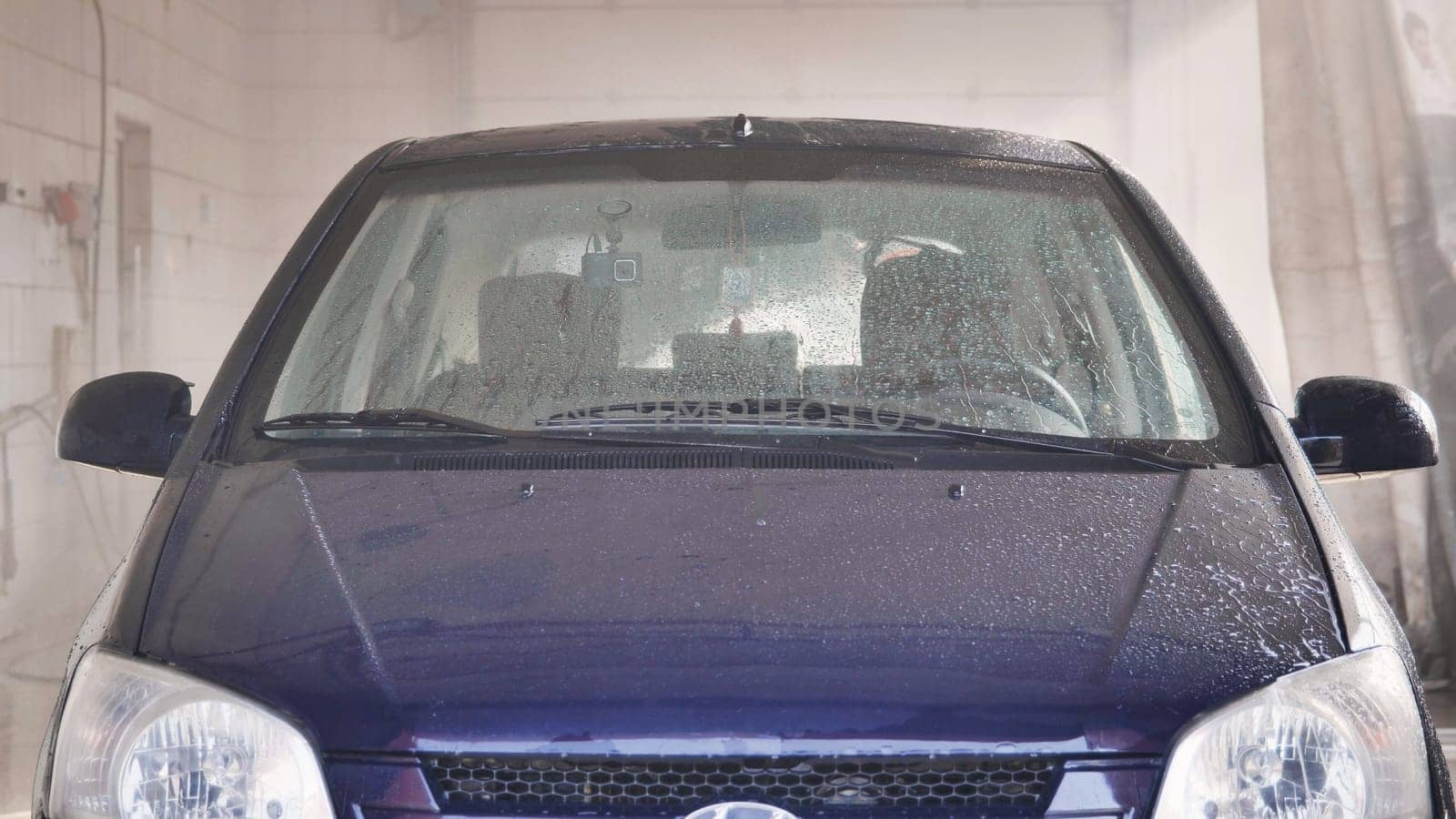 Car getting washed in automatic car wash with soap foam and water spraying on windshield