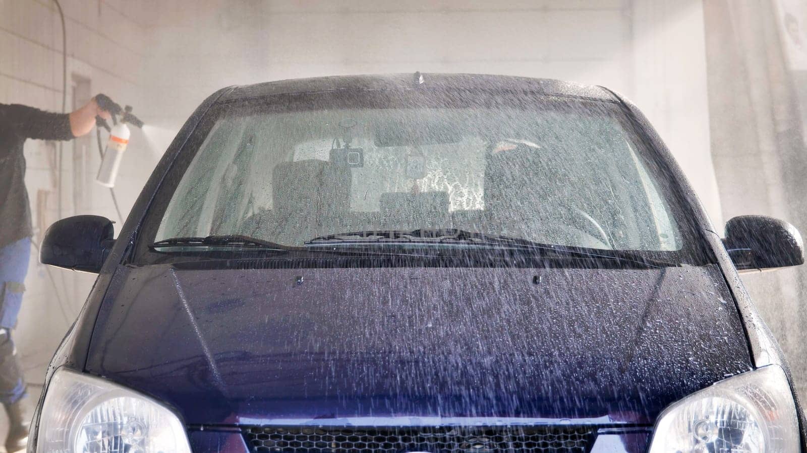Car wash worker spraying foam on a vehicle with a high pressure water jet