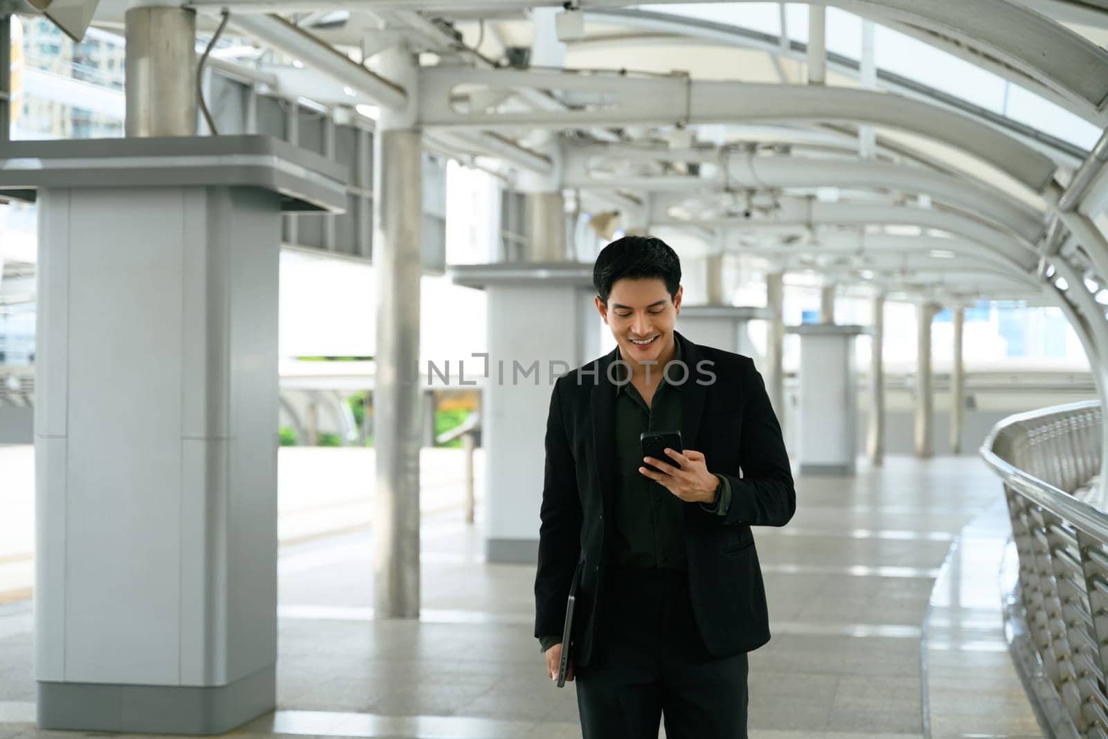 Confident businessman using smartphone walking in modern city walkway.