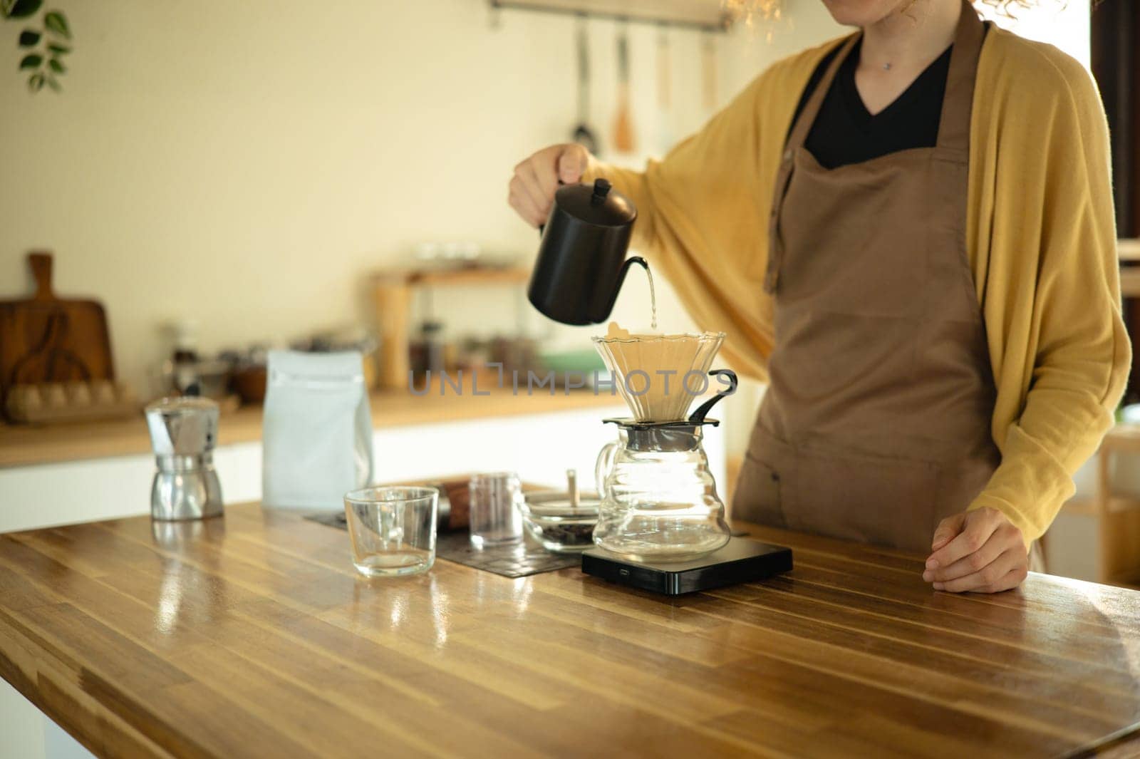 Cropped shot of woman pouring hot water into dripper, preparing pour over coffee at home.