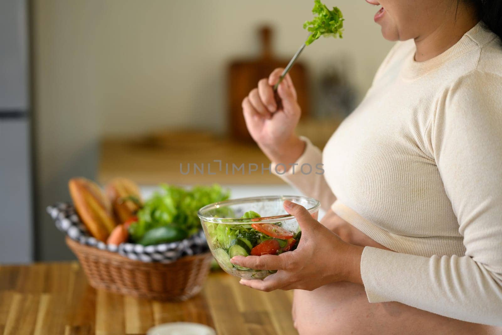 Expectant mother enjoying a vegetable salad in a kitchen, balanced diet for prenatal health.