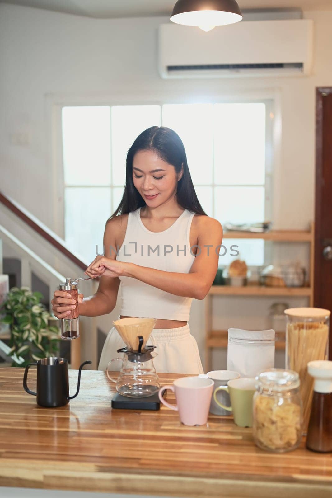 Asian woman preparing pour over coffee with fresh beans and mugs on the counter.