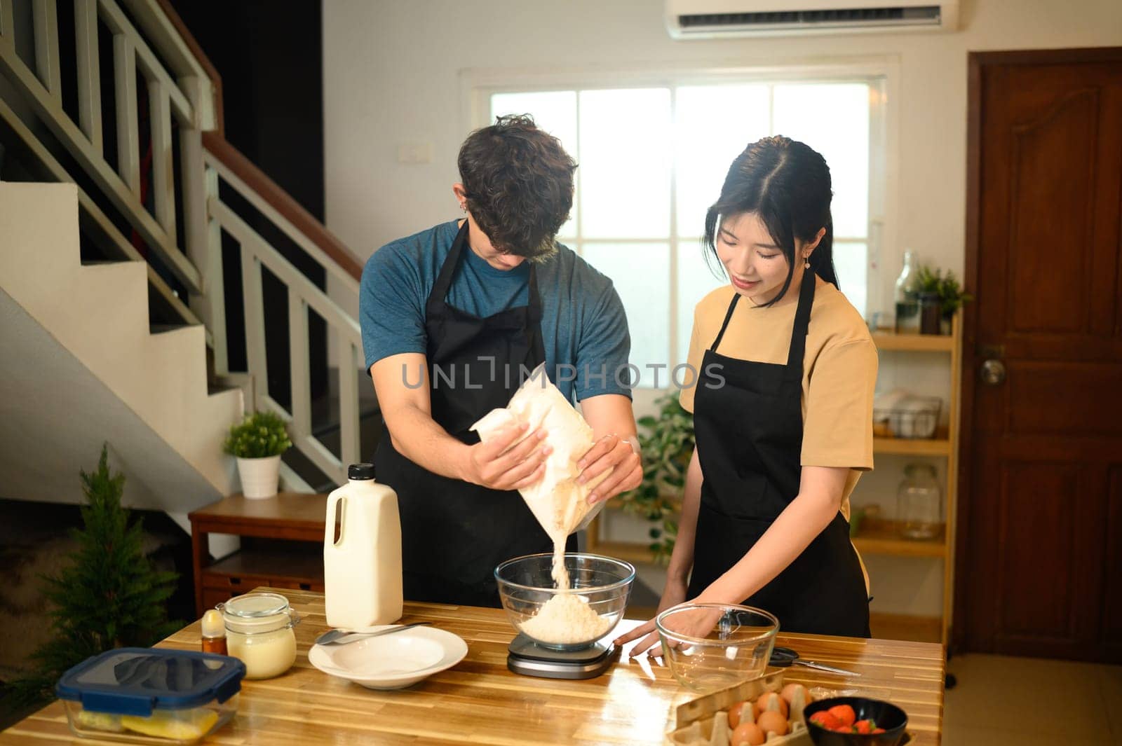 Young couple preparing pancake batter together in a kitchen.