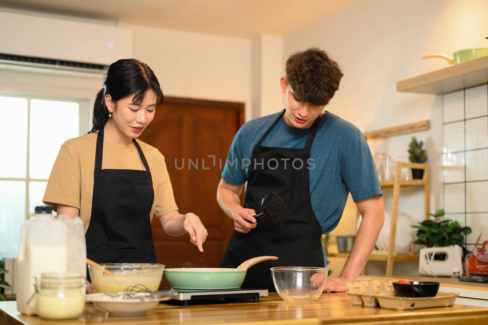 Happy young couple in aprons preparing to cook pancakes in a cozy home kitchen.
