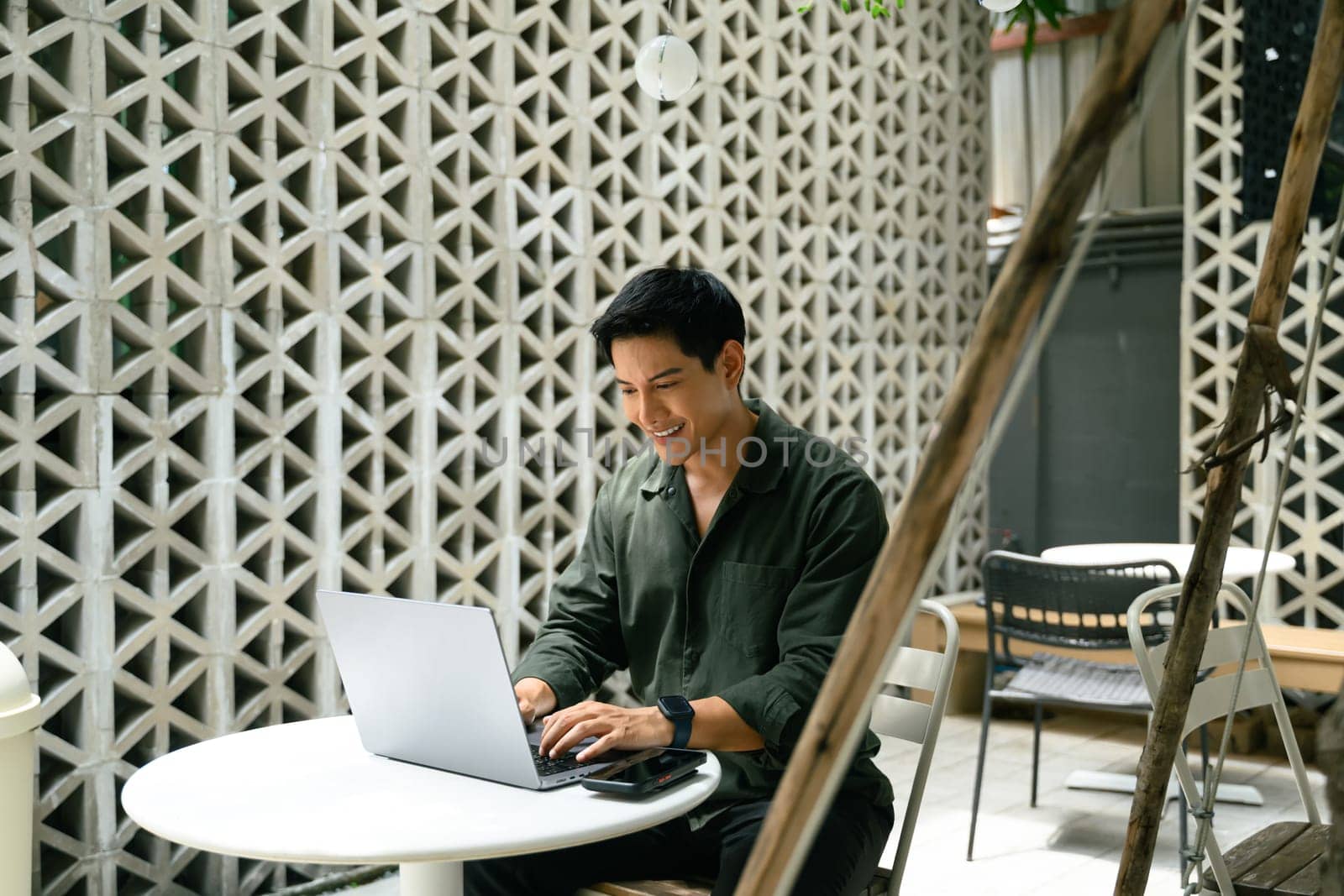 Smiling man working remotely on a laptop at a modern outdoor cafe.