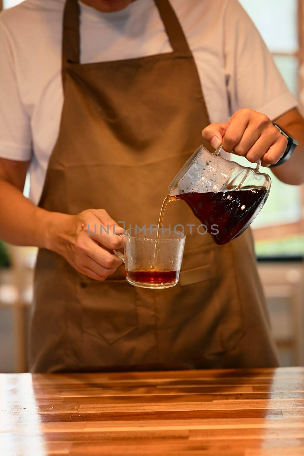 Cropped shot of man pouring fresh brewed coffee into glass cup in a kitchen.