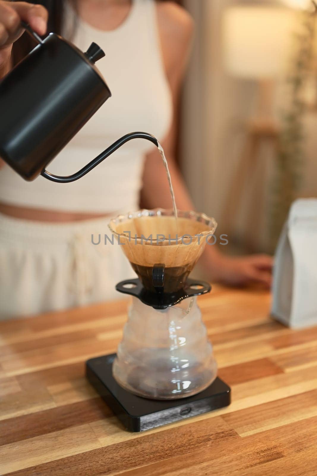 Close up of a woman pouring hot water into a pour-over coffee filter at home.