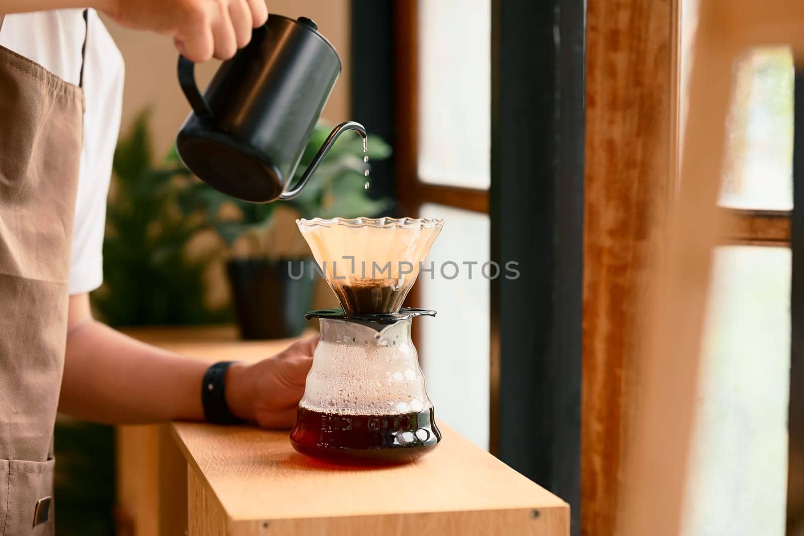 Close up of man brewing coffee with pour over method using a glass dripper in a kitchen.
