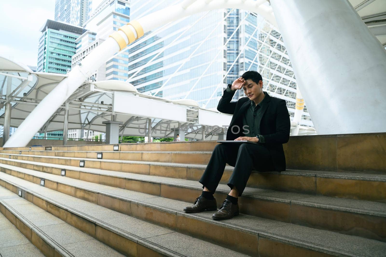 Businessman sitting on outdoor steps, looking tired and overwhelmed from work stress.