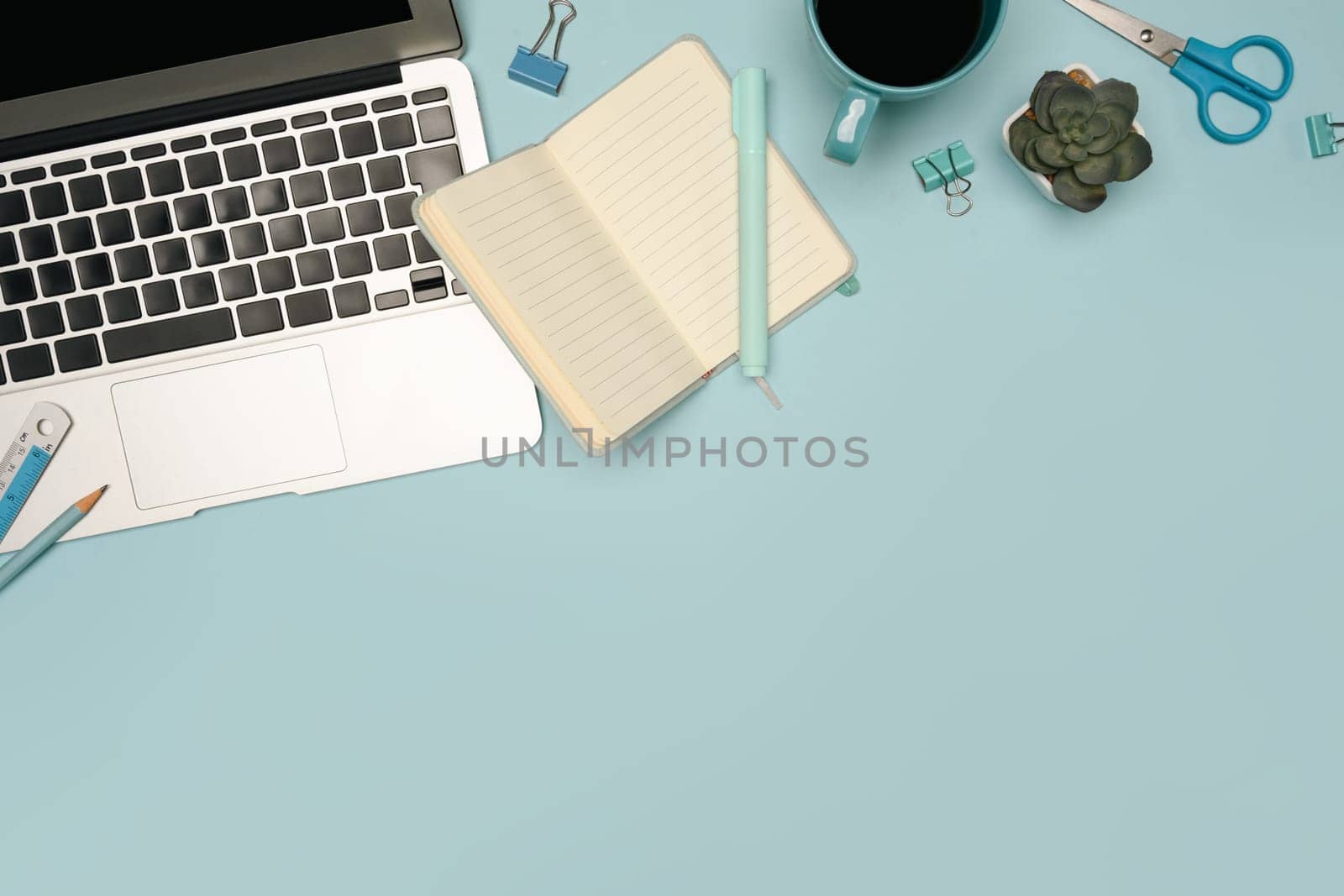 Flat lay of creative desk setup with office supplies and laptop on pastel blue background.