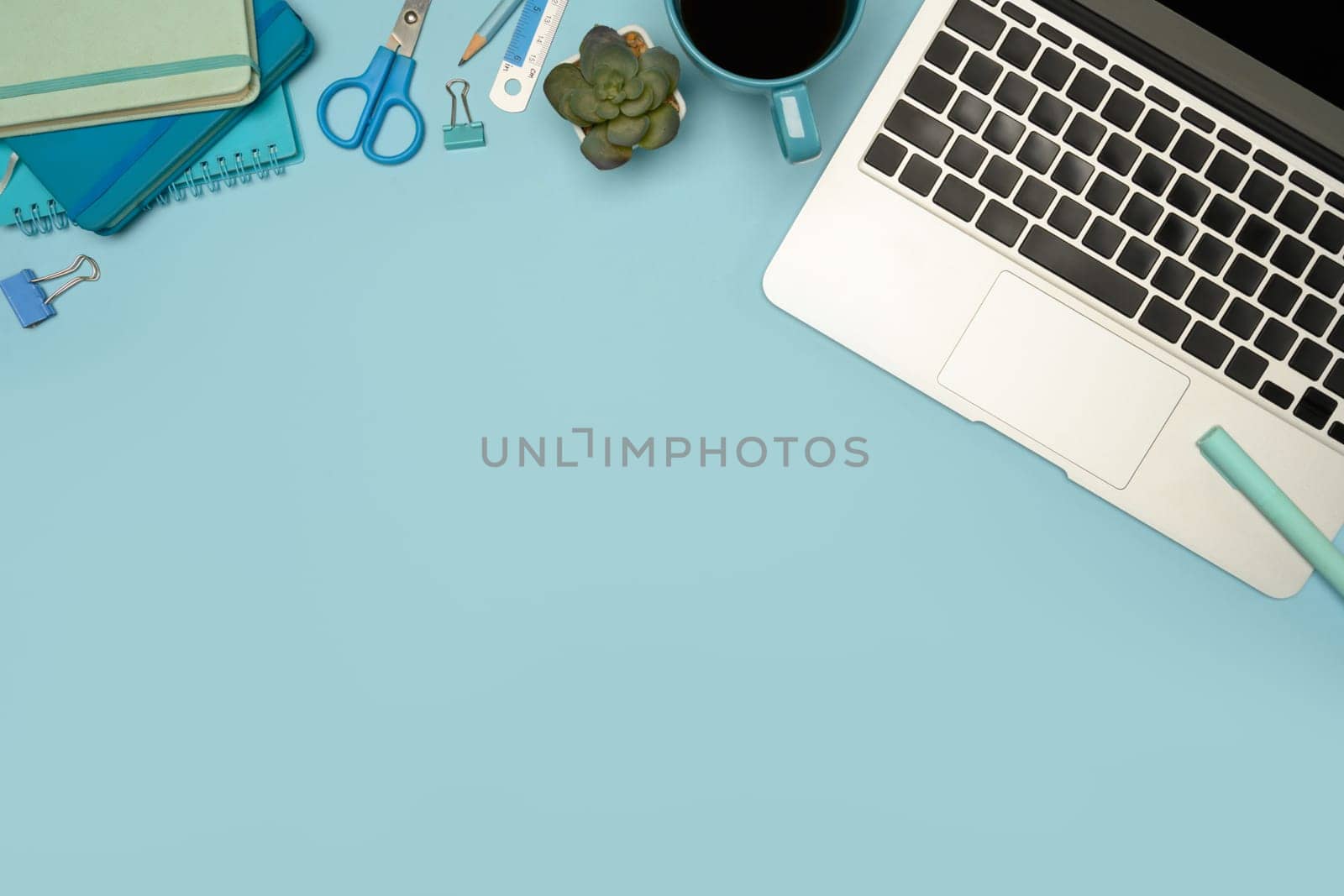 Top view of modern workspace with laptop, stationery and coffee cup on pastel blue background.
