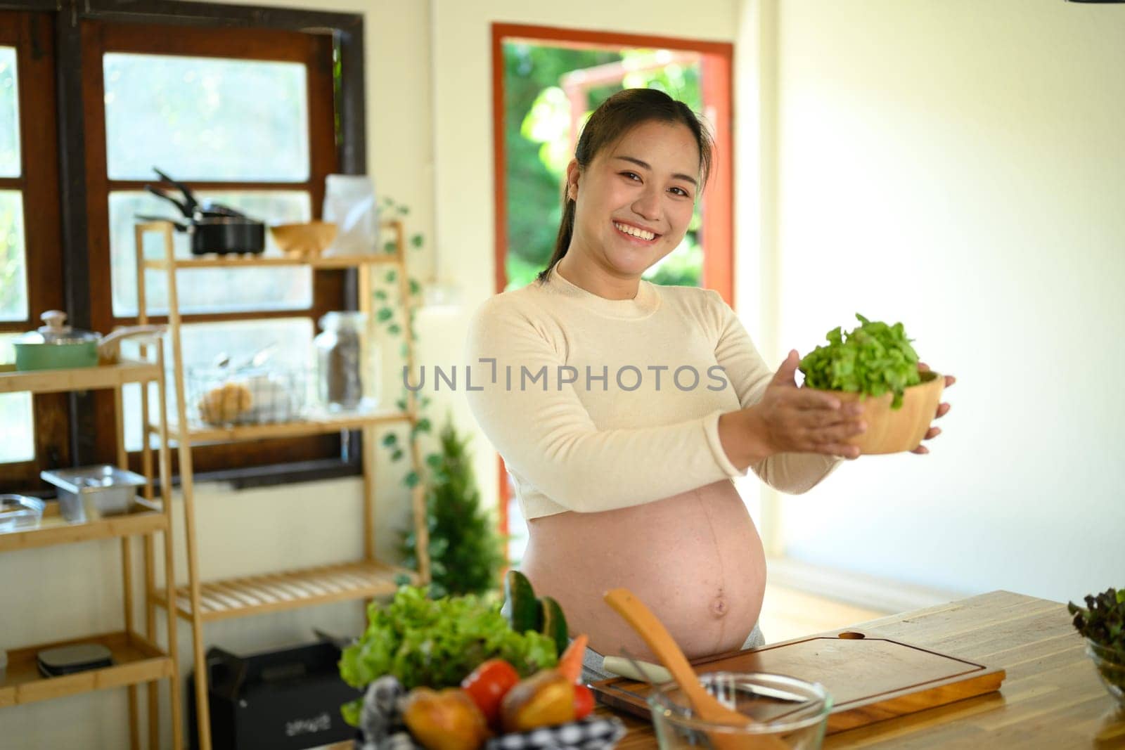 Happy pregnant woman preparing a nutritious meal with fresh ingredients in home kitchen.