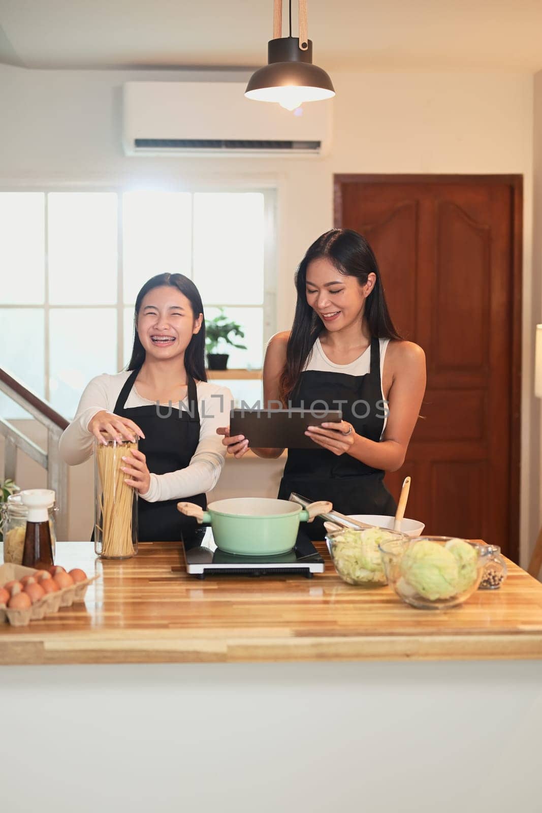 Beautiful asian mother and daughter cooking pasta together in the kitchen.