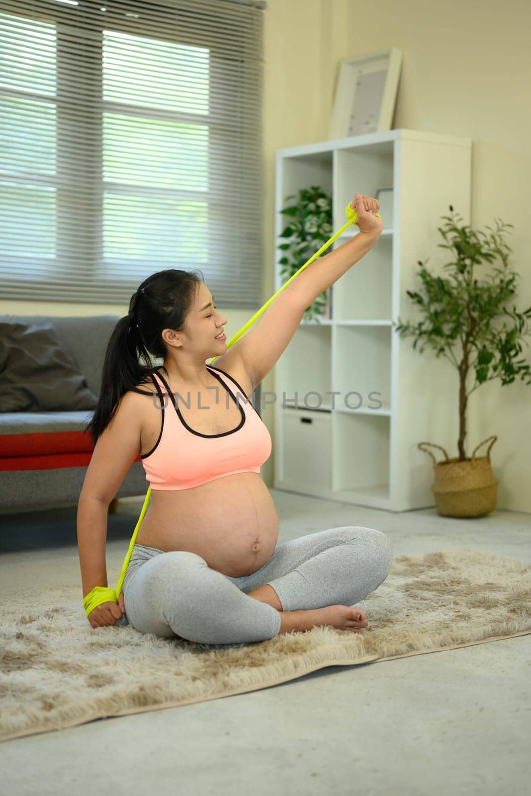 Smiling pregnant woman doing a home workout with a stretch band.