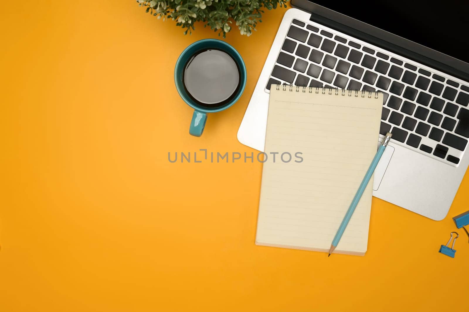 Flat lay of modern desk with a coffee cup, laptop and notebook on yellow background.