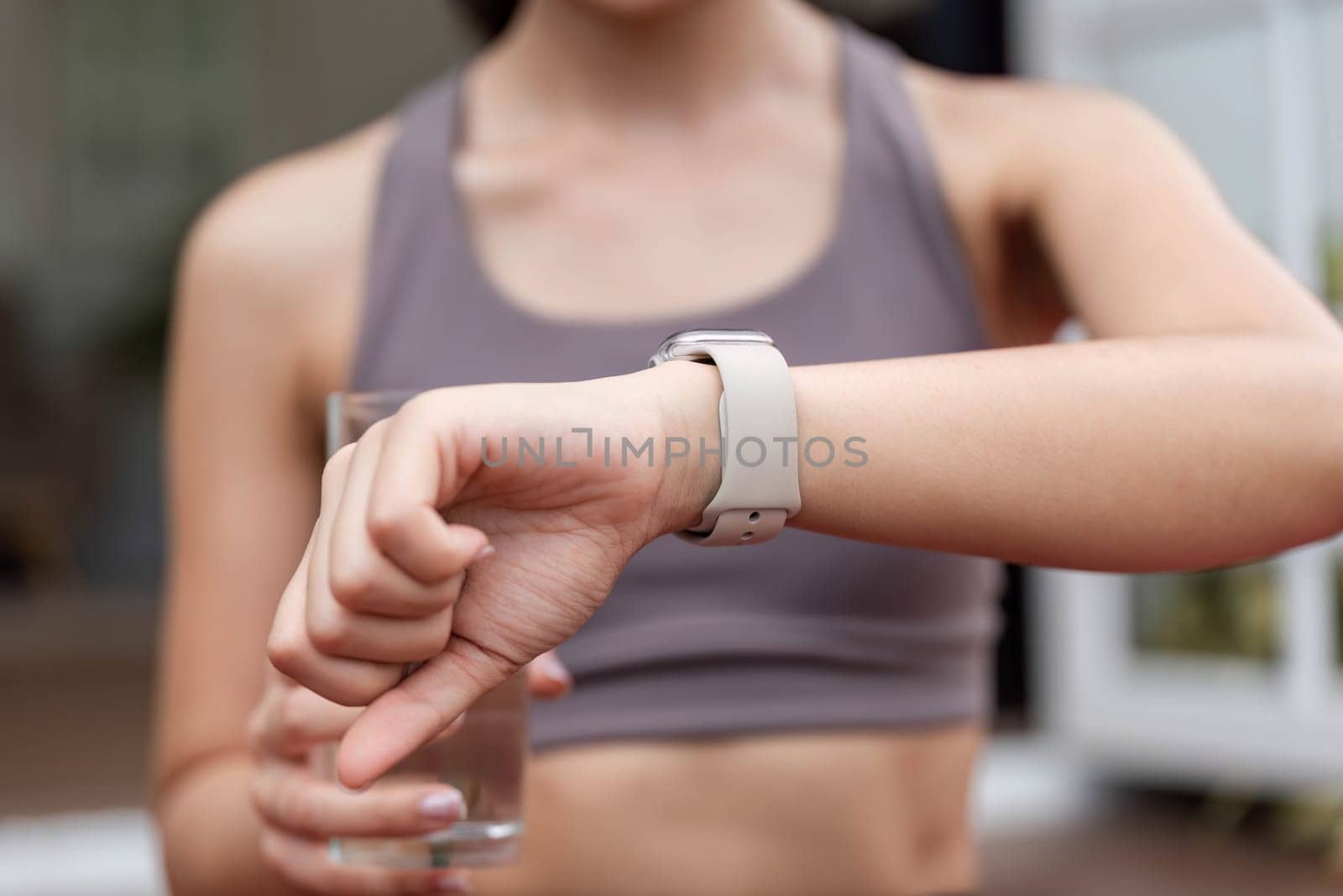 A young woman checks her smartwatch for fitness updates, holding a glass of water, emphasizing health and hydration.