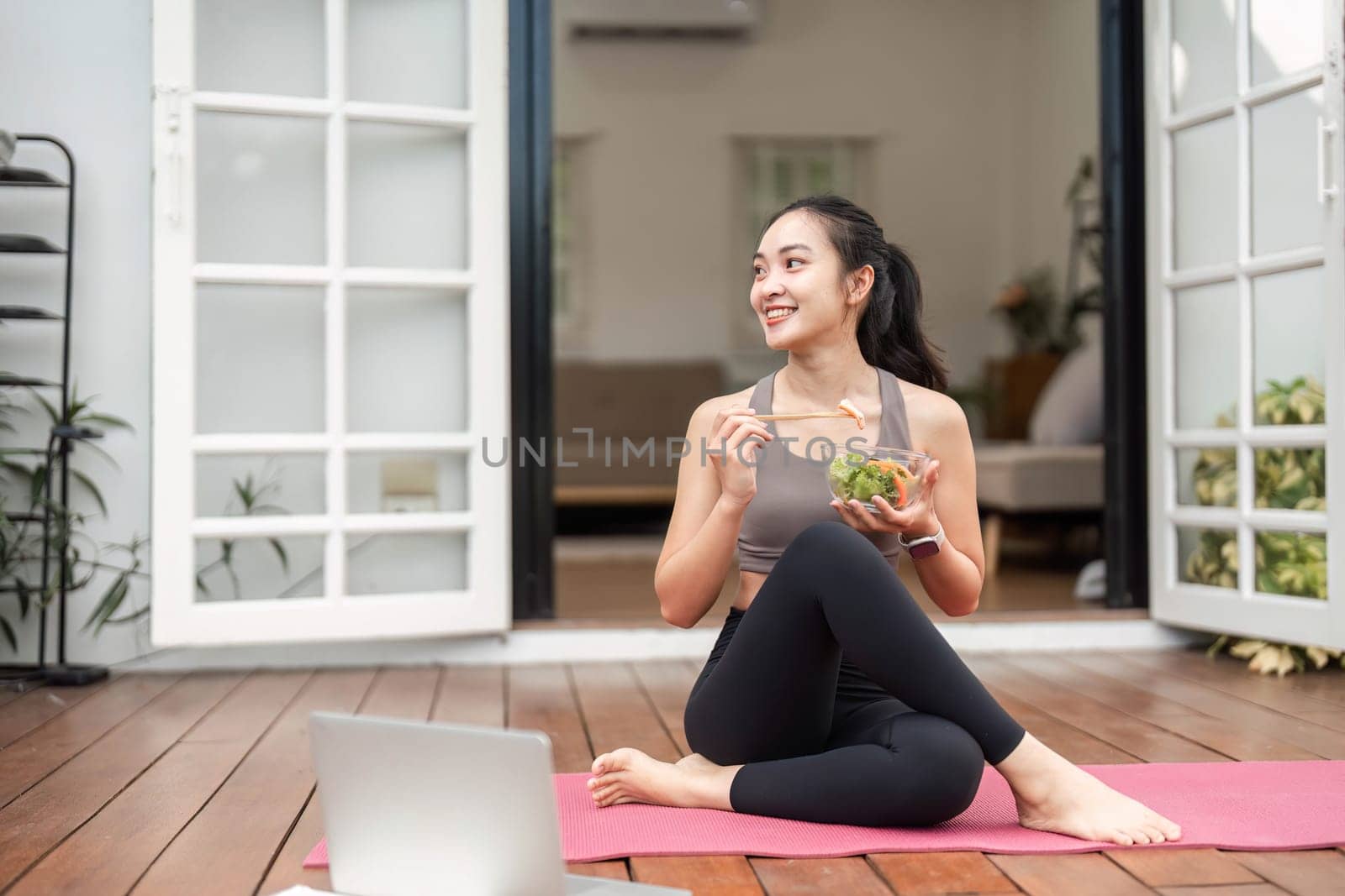 A woman sitting on a yoga mat, savoring a fresh salad, emphasizing the connection between healthy eating and fitness.