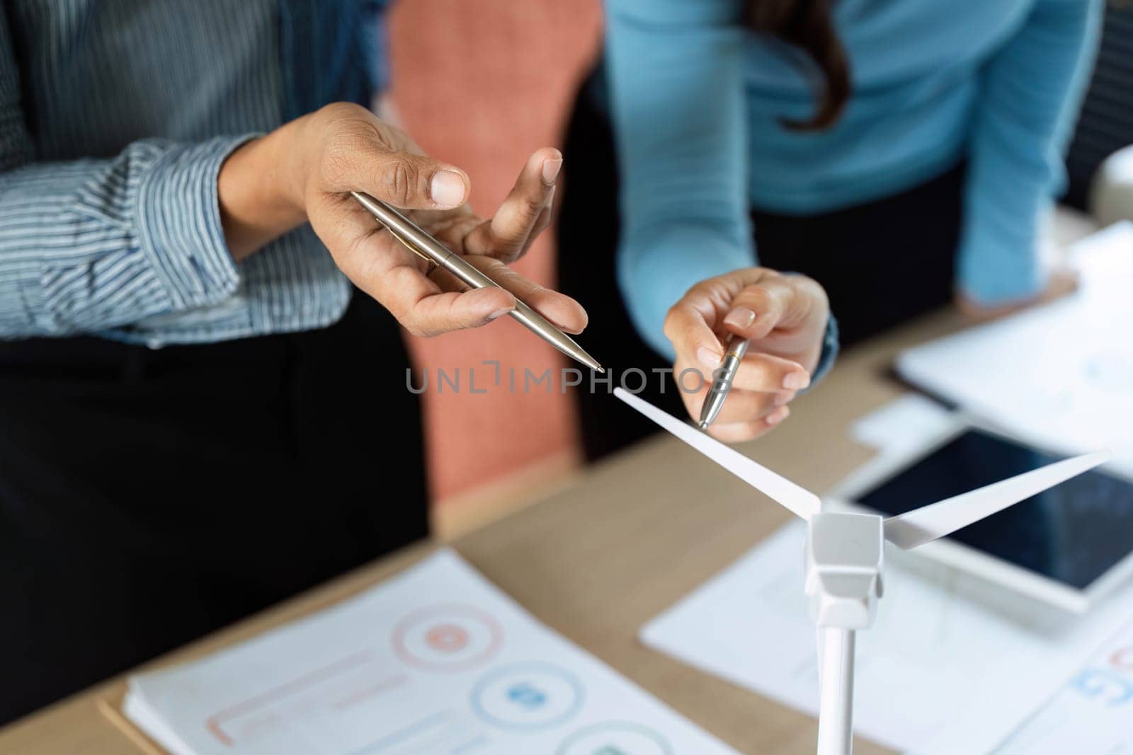 Two business professionals engage in a discussion about renewable energy strategies, focusing on a wind turbine model to emphasize sustainability.