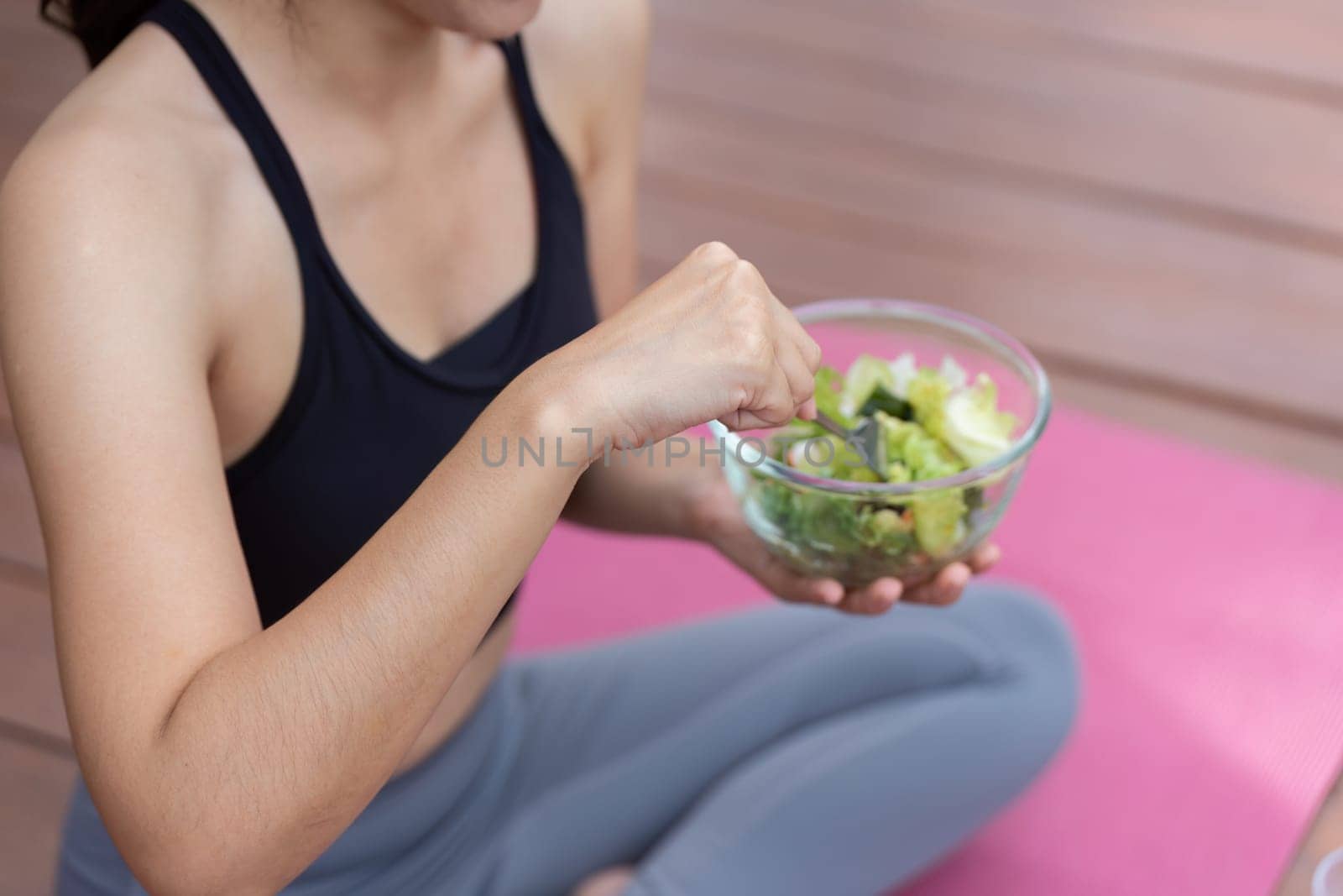 A health-conscious woman enjoys a nutritious salad on a yoga mat, highlighting the importance of healthy eating.