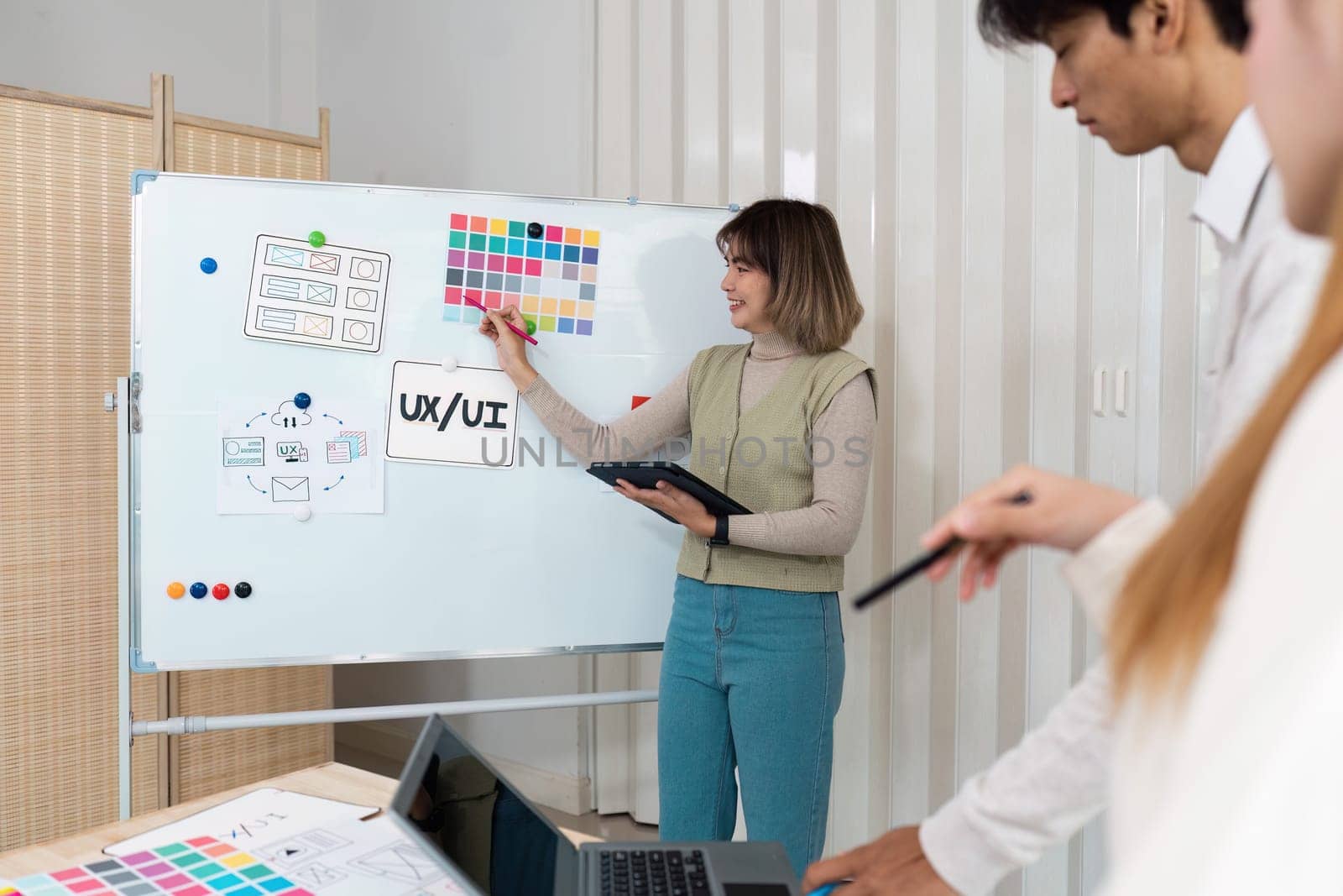 In a professional setting, a woman outlines UX UI ideas while her colleagues engage in the creative brainstorming process, showcasing collaboration and innovative thinking.