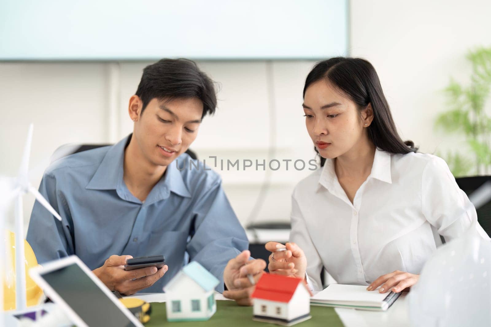 Two engineers collaborate on sustainable architecture, analyzing eco-friendly designs with miniature models and digital tools, highlighting innovation in construction.