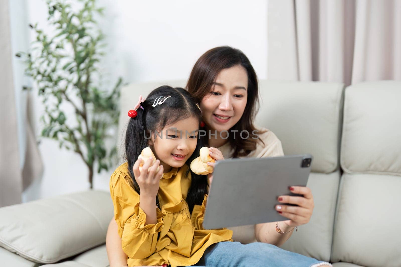 The mother and daughter share a delightful moment as they engage with a tablet, showcasing their close relationship and modern family life.